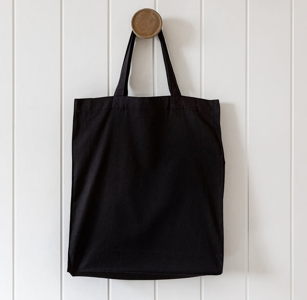 Black tote bag hanging on a wooden hook against a white wooden panel background