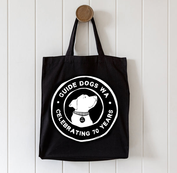 Black tote bag with Guide Dogs WA logo on a white wooden background