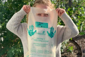 Child holding Expressions Tea Towels’ 100% compostable packaging bag in front of their face, standing in a leafy backyard garden