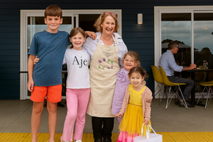 Smiling woman wearing a customised apron standing with happy children outside a café—perfect example of personalised apron gifting in Australia.