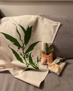Organic cotton tea towel with green leaf print and eco gift wrap on sofa showing sustainable tea towels Australia style