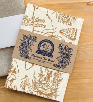Souvenir tea towel with floral artwork and branded kraft wrap packaging, printed on organic cotton and made in Australia
