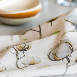 Close-up of a printed tea towel with a soft, botanical cotton design on natural fabric, styled next to ceramic bowls on a kitchen bench.