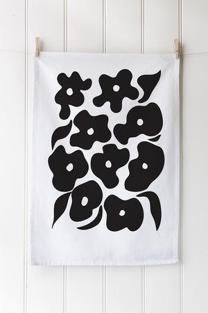 White cotton tea towel with black floral pattern hanging on white wall