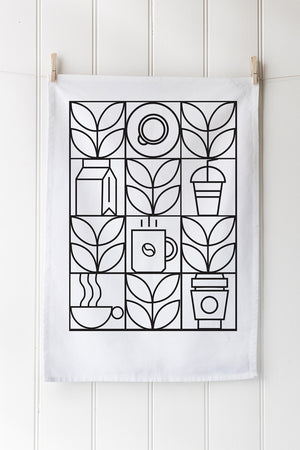 White tea towel with black geometric coffee-themed pattern hanging on a wooden wall.