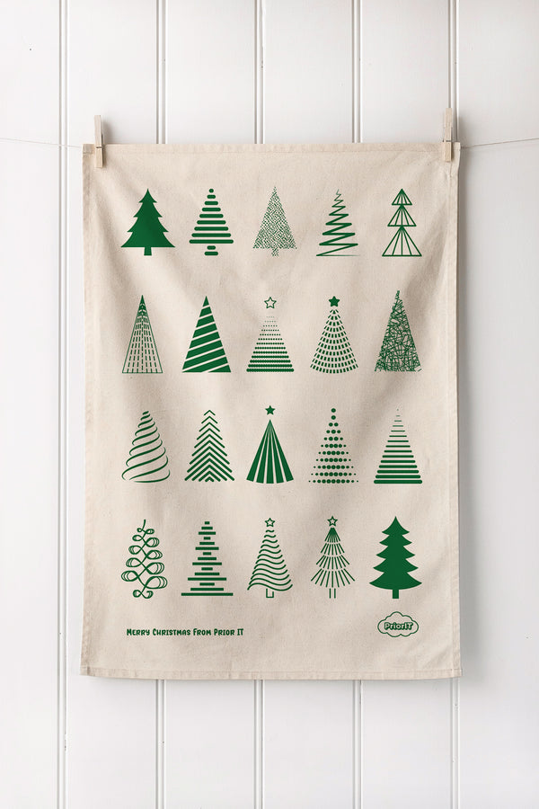 Natural tea towel with Bottle Christmas tree patterns hanging on a white wall.