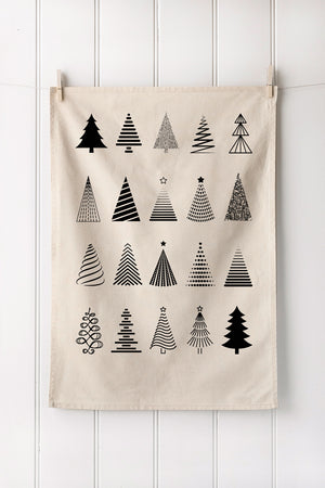 Natural cotton tea towel with black Christmas tree patterns hanging on a white wooden panel wall.