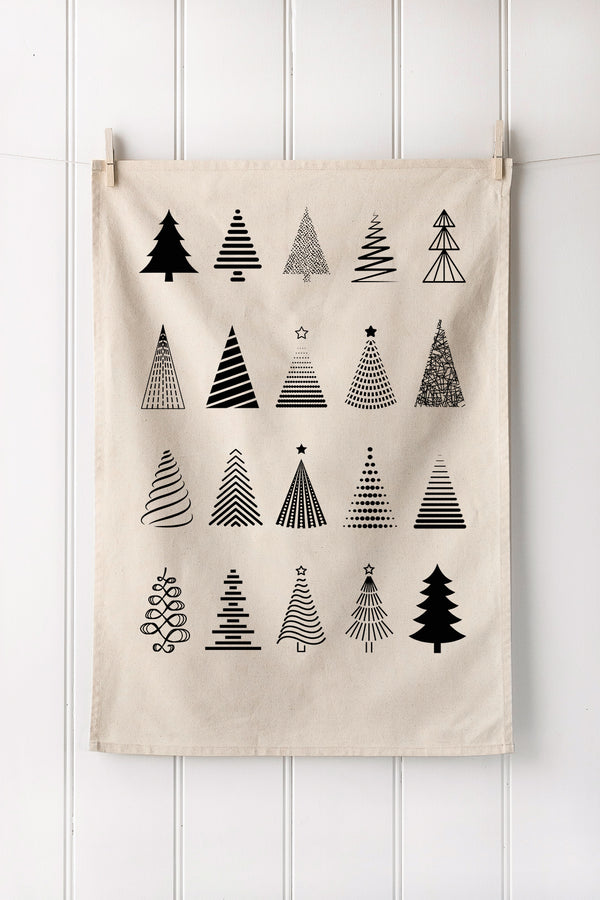 Natural cotton tea towel with black Christmas tree patterns hanging on a white wooden panel wall.
