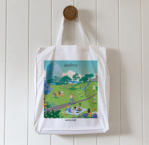 White tote bag with a colorful graphic design hanging on a wooden hook against a white paneled wall.
