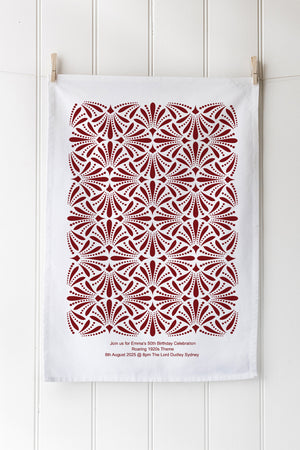 White tea towel with red geometric pattern hanging on a wooden rack.
