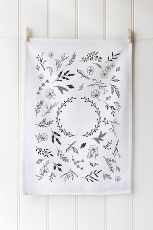 White tea towel with fauna wreath print hanging on a white wall