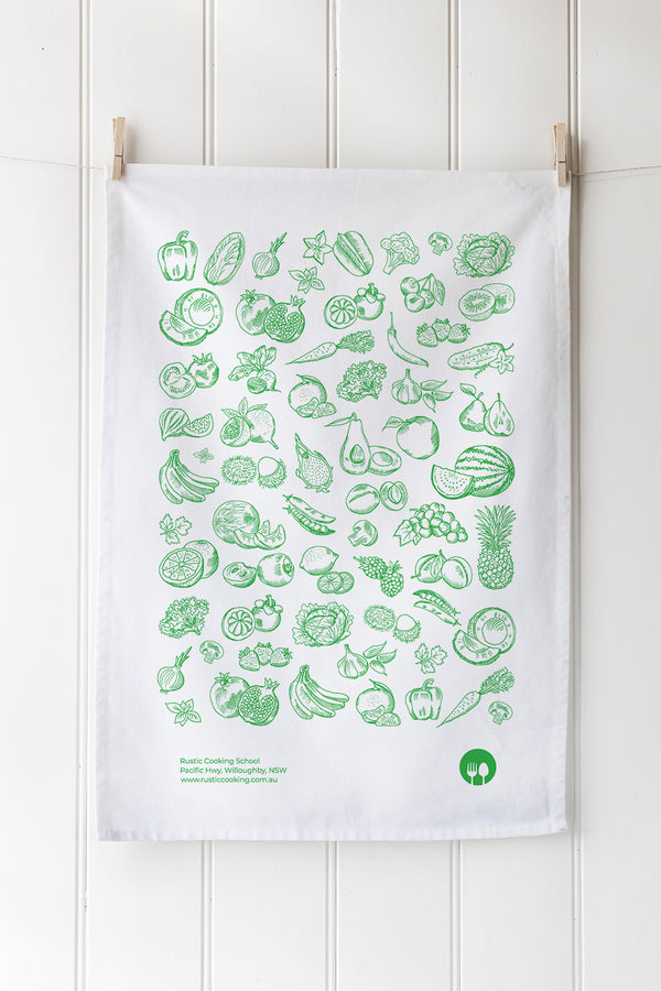 White cotton tea towel with green vegetable illustrations hanging on a wooden rack.