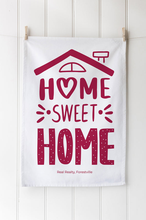 White cotton tea towel with red 'Home Sweet Home' with real estate branding design hanging on a white wooden wall.
