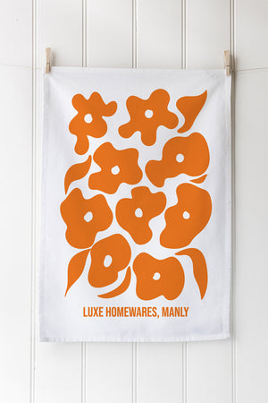 White tea towel with orange floral pattern and customisable text on a white background