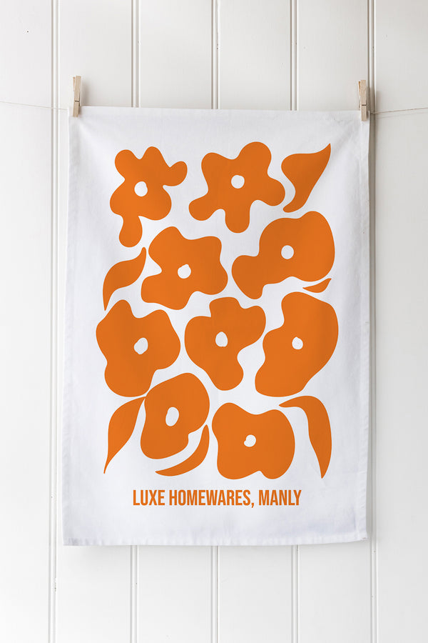 White tea towel with orange floral pattern and customisable text on a white background