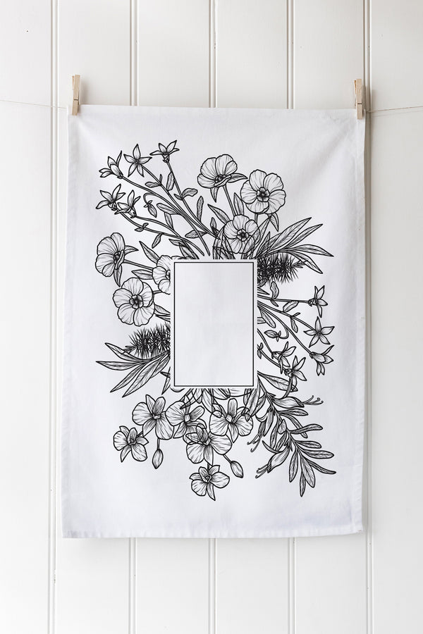 Floral design on a white tea towel hanging against a white wooden panel background