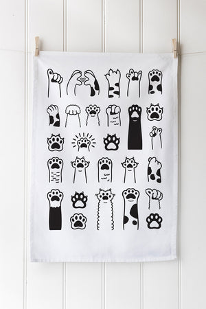 White tea towel with black paw print designs hanging on a wooden wall.