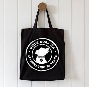 Black tote bag with Guide Dogs WA logo on a white wooden background