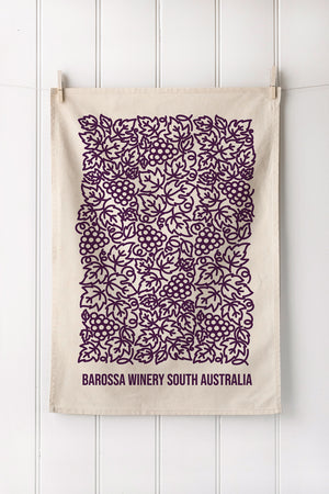 Natural cotton tea towel with purple vineyard pattern and text on a white wooden background