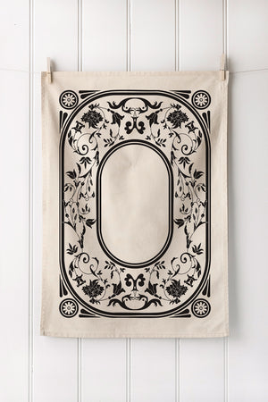Decorative fabric panel with black floral and leaf pattern on a white wooden background
