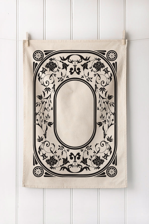 Decorative fabric panel with black floral and leaf pattern on a white wooden background