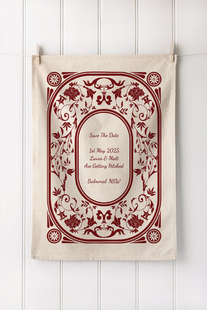 Wedding save the date tea towel with burgundy floral design on a white wooden background