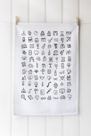 White tea towel with black wedding illustrations hanging on a white wall.