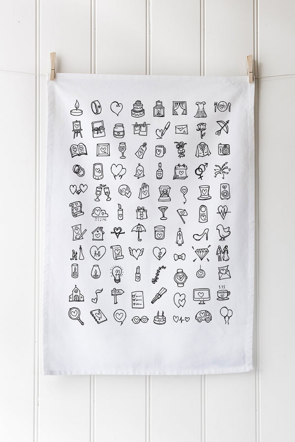 White tea towel with black wedding illustrations hanging on a white wall.